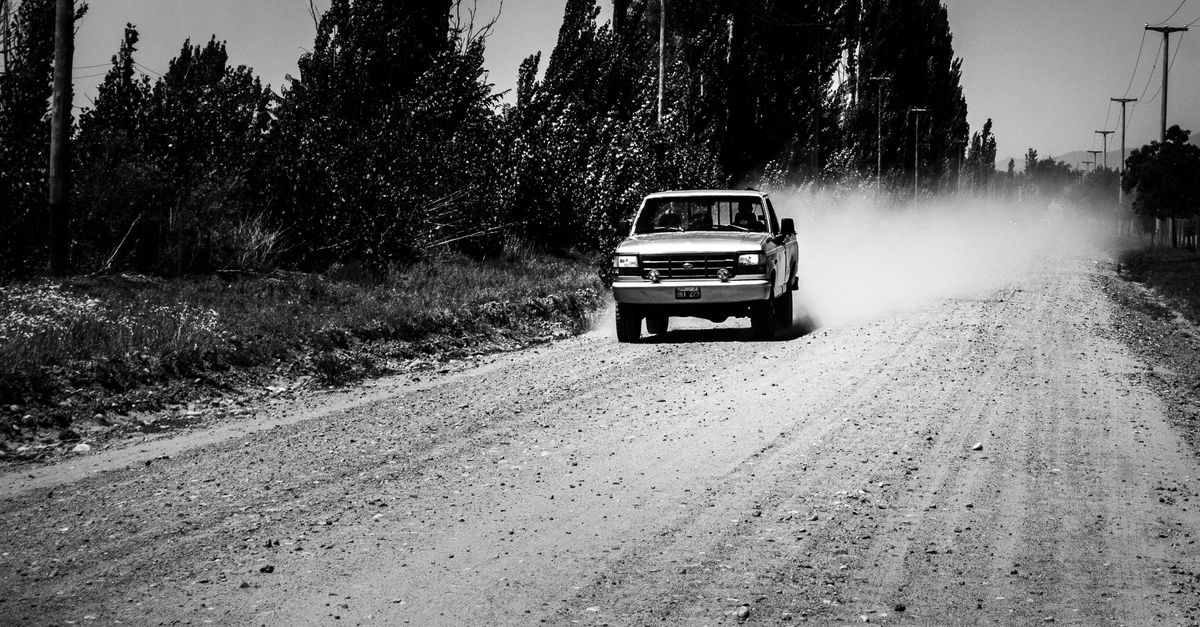 Pickup circulando por un camino de ripio con polvo levantado